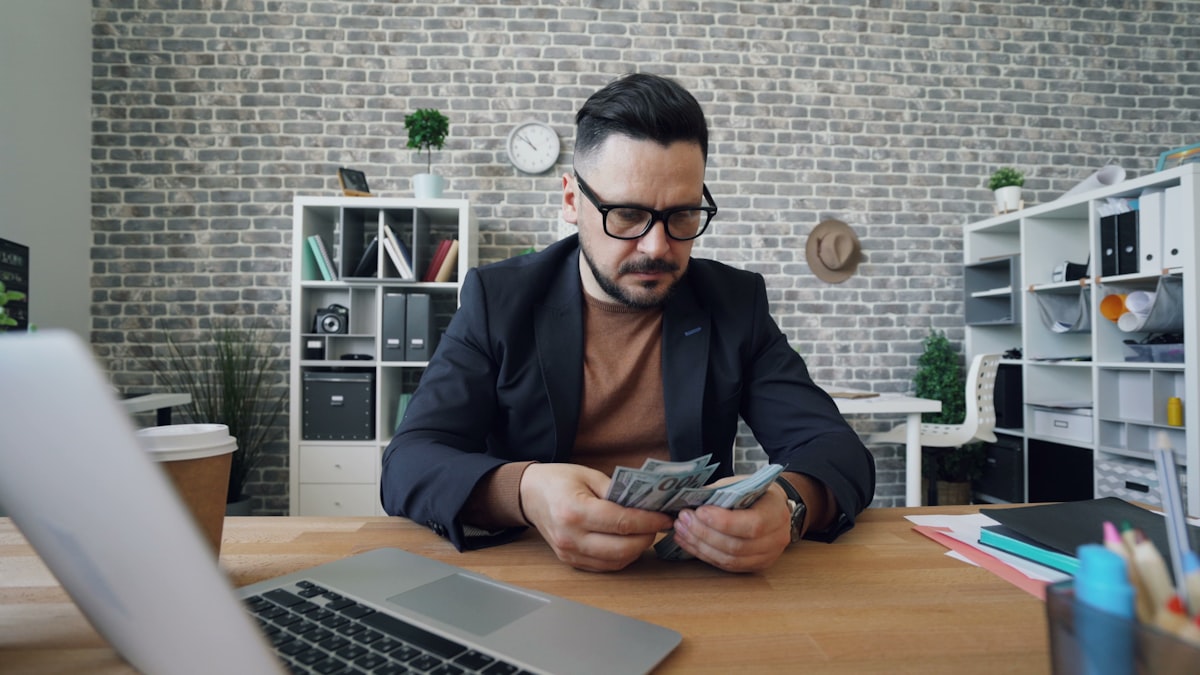 Man at desk counting US dollar bills while reviewing eviction costs