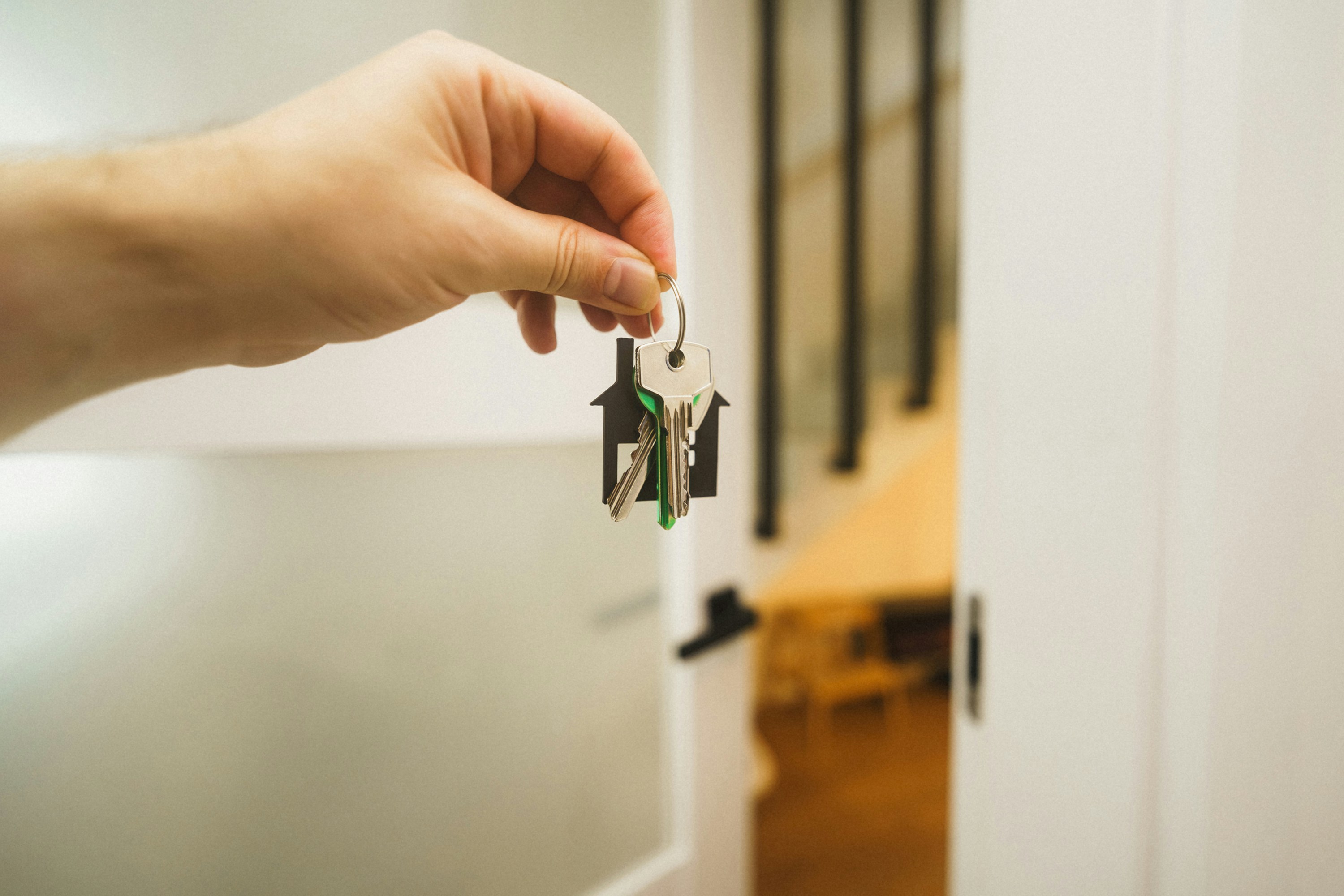 A hand holding a key to a front door of a property